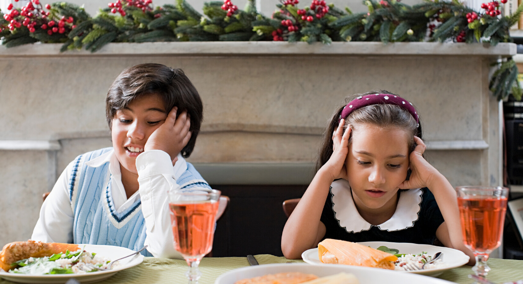 Boy and girl sitting a fancy Christmas dinner not looking happy.