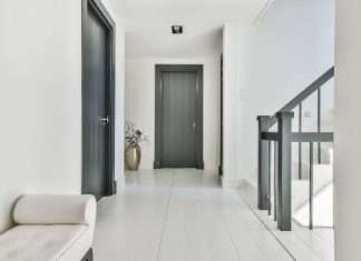 An elegant white hallway facing the front of a house. The doors and stair railings are a dark gray color.