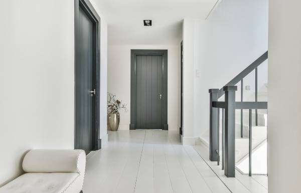 An elegant white hallway facing the front of a house. The doors and stair railings are a dark gray color.