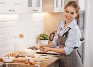 A woman standing at a kitchen counter that has flour, a rolling pin, and broken eggs on it as she holds dough in her hands.