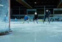 A hockey practice on an indoor rink. Players practice in the background while two young players skate toward the goal next to their coach.