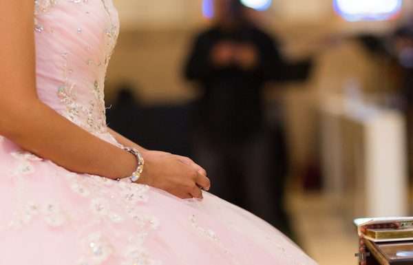 The side profile of a woman from the neck down in a poofy, pale pink gown with a book and rosary sitting in front of her.