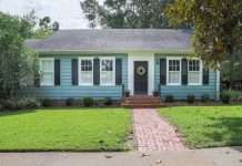 The exterior of a blue, one-level home with a small front yard and a wreath on the door. The yard has minimal landscaping.