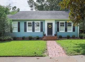 The exterior of a blue, one-level home with a small front yard and a wreath on the door. The yard has minimal landscaping.