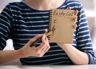 A close-up of a woman holding a notebook page that reads, "To-Do List" and "1, 2, 3." She has a pen pointed to the page.