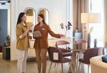 A female shopper standing with a female furniture store sales associate. The associate is pointing to a dining set.