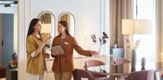 A female shopper standing with a female furniture store sales associate. The associate is pointing to a dining set.