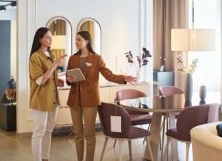 A female shopper standing with a female furniture store sales associate. The associate is pointing to a dining set.