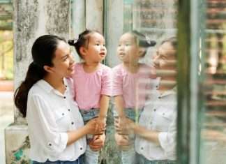 A mother holds up her small child so that she can look through a glass wall at a zoo. Both are smiling.