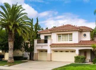A two-story house in California. Behind the house, there is a semi-clear sky, and there is a palm tree on the lawn.