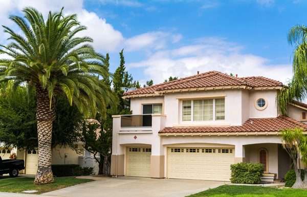 How Different Building Codes Affect Your Family Home A two-story house in California. Behind the house, there is a semi-clear sky, and there is a palm tree on the lawn.