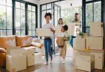 What To Consider When Moving to California With Your Family A family of two adults and two children is walking into a home with large windows and stacks of moving boxes.