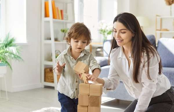 A mother and child playing with blocks in a well-lit living room. The child is placing a block on the tower.