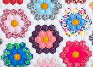 A close-up of a beautifully crafted quilt that has patches of flowers against a white background. Each flower is a different color and pattern.