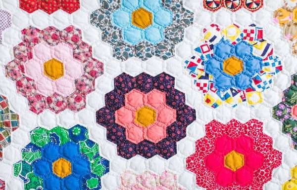 A close-up of a beautifully crafted quilt that has patches of flowers against a white background. Each flower is a different color and pattern.