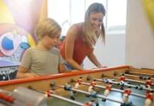 Community Game Nights That Bring Families Together A woman and a young boy smile while playing foosball together at a table in a bright indoor recreation area.