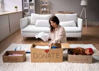 A woman sits on the floor in front of a white couch and sorts clothing into boxes labeled, "Keep," "DONATE," and "Discard."